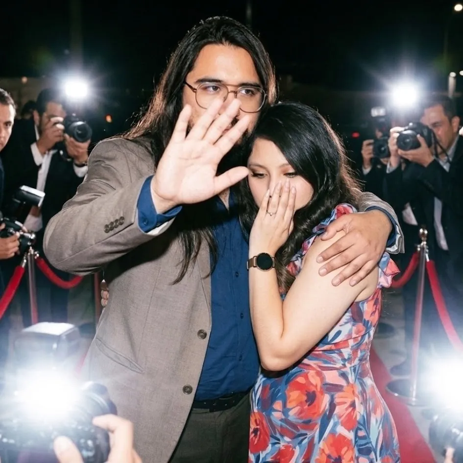 Jesse Lopez and Meli smiling together as photographers take pictures at an evening event